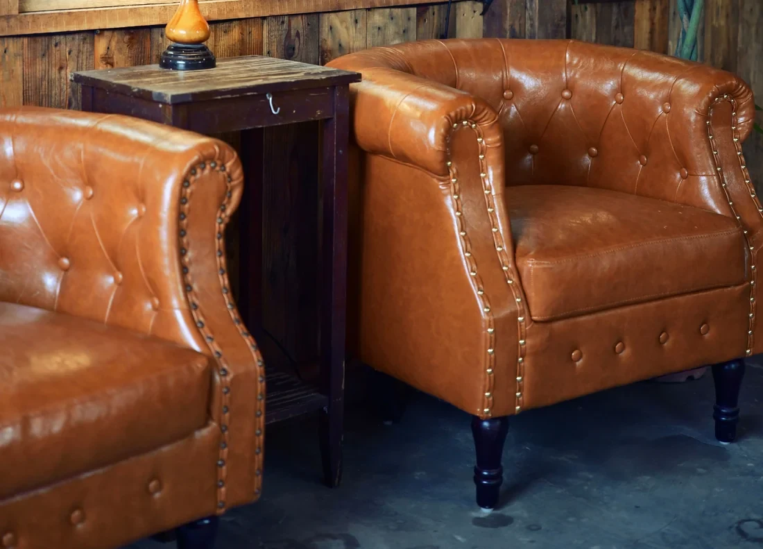 Two tan buttoned leather club chairs beside a side table